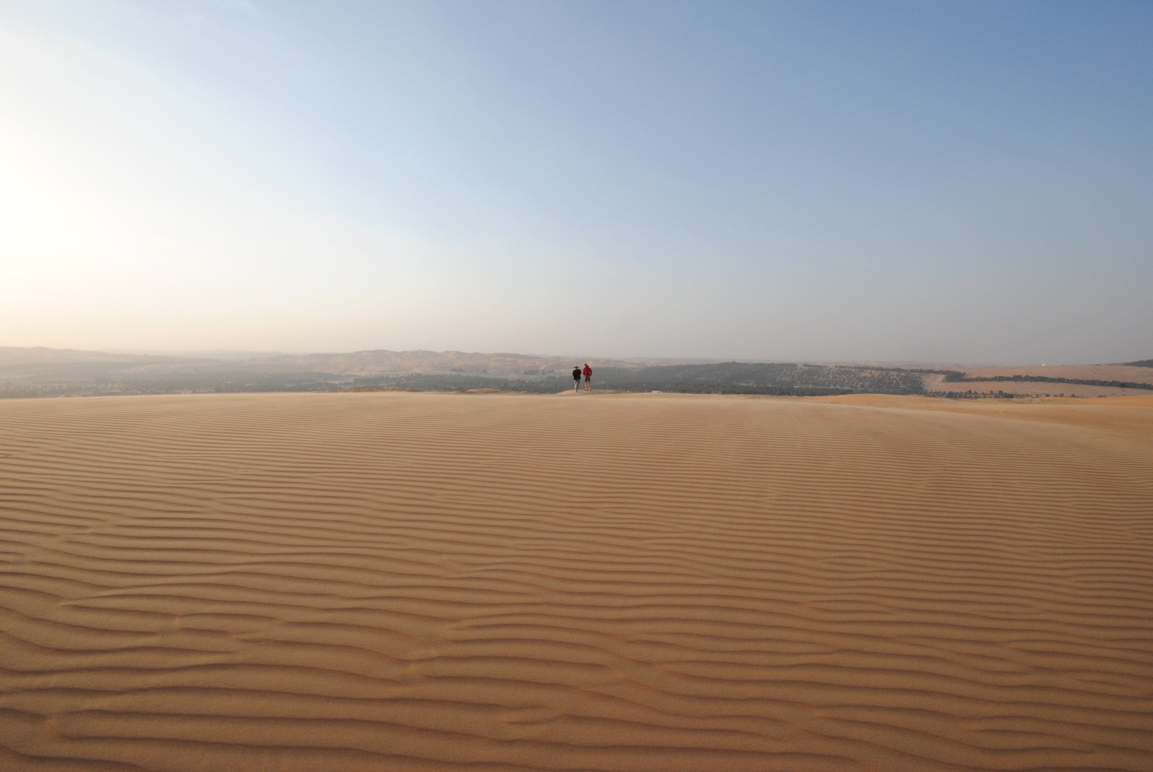 Vast open dunes with two distant figures on the horizon