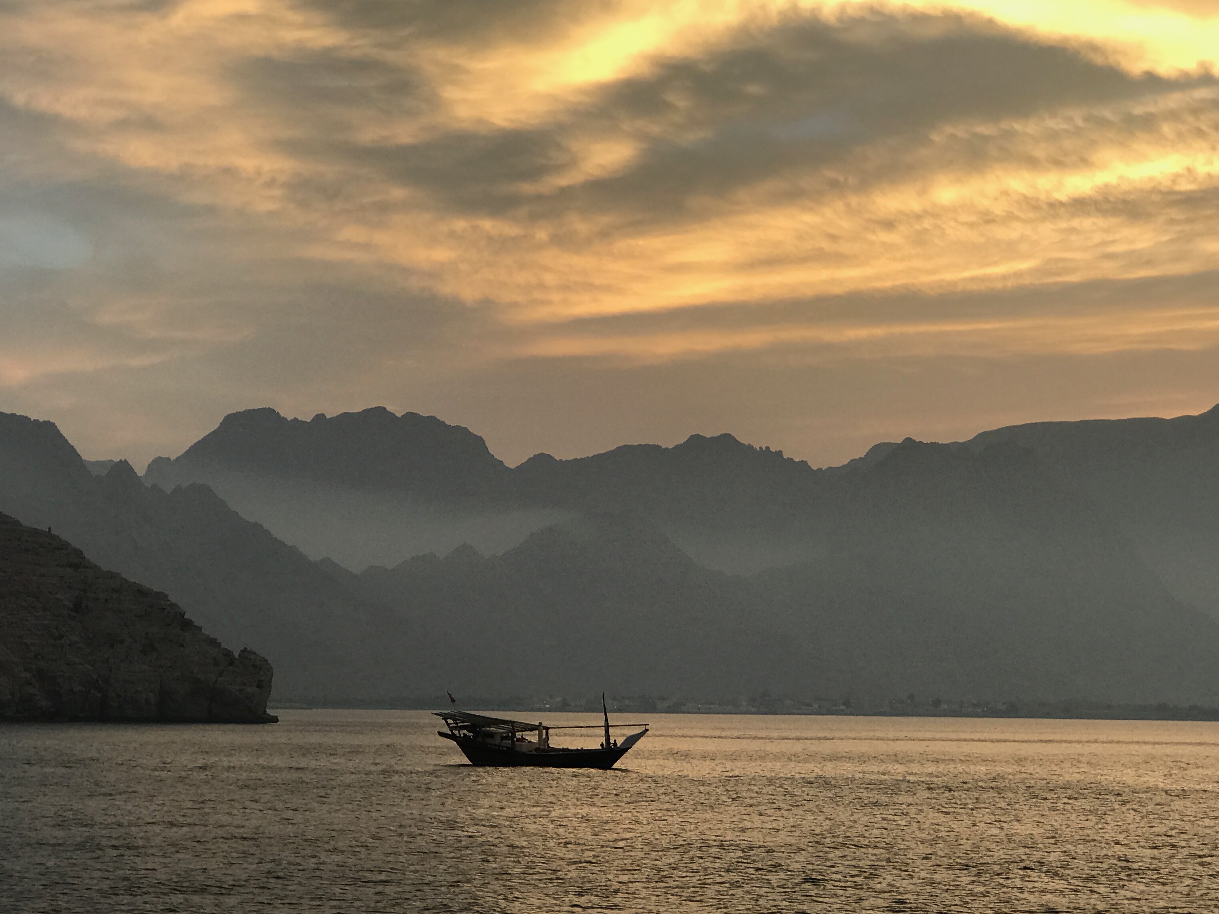 A boat at dusk on calm water below distant mountains